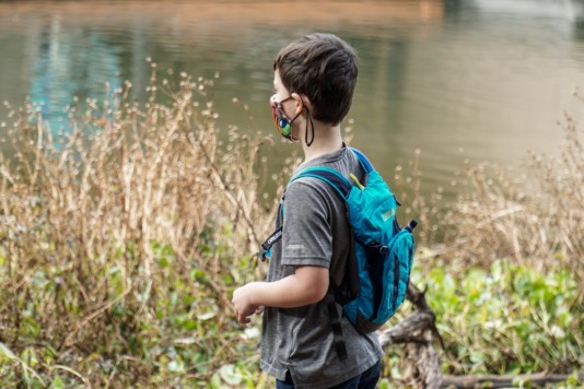 Young boy hiking in nature with a camelbak and wearing a mask during the COVID-19 pandemic.